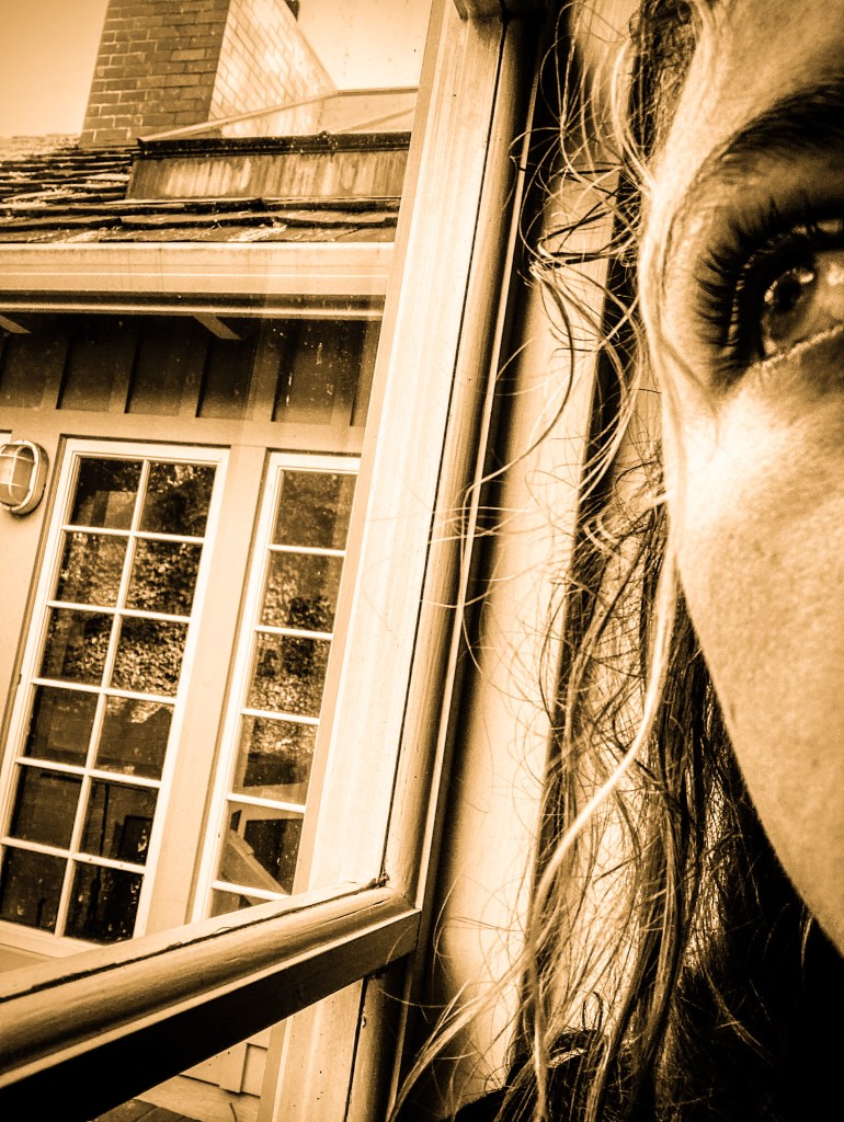 A photograph of the author looking out a window as a metaphor for being stuck behind the glass of who we really are. 