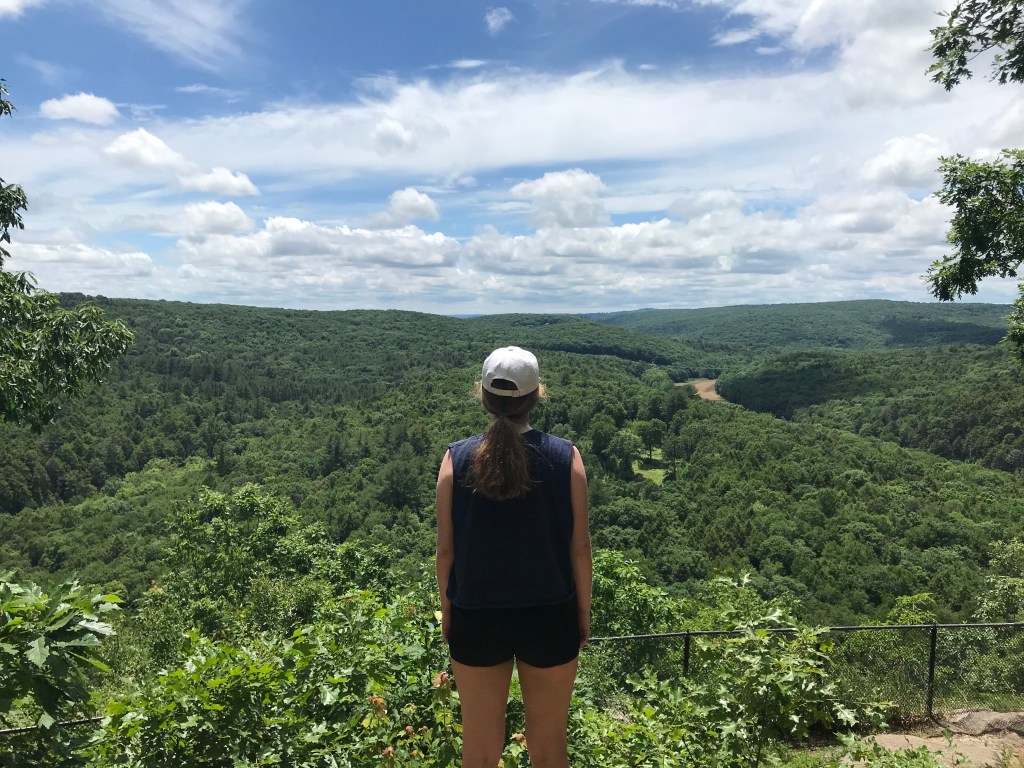 Photograph of the author looking over over a sweeping view of the Western Connecticut foothills, celebrating her strength. 