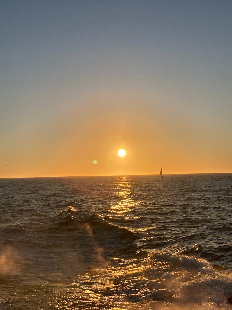 A sailboat sails off into the sunset on the Pacific Ocean. 