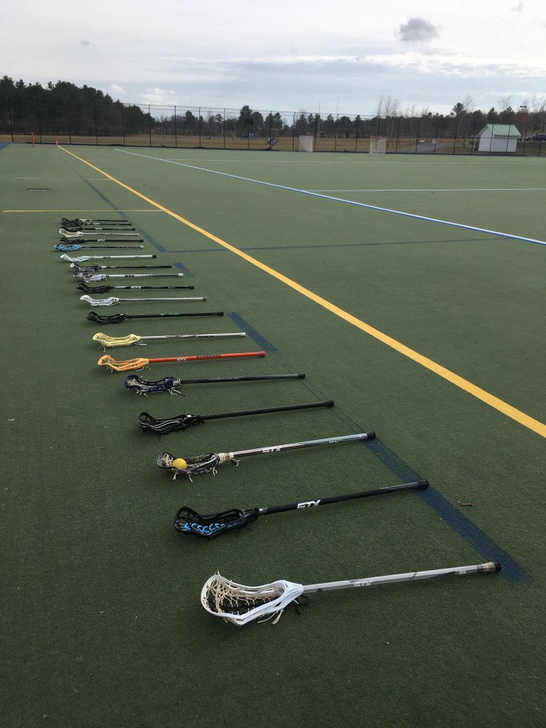 Photograph of lacrosse sticks lined up on the sidelines, taken by a player sidelined by injury. 