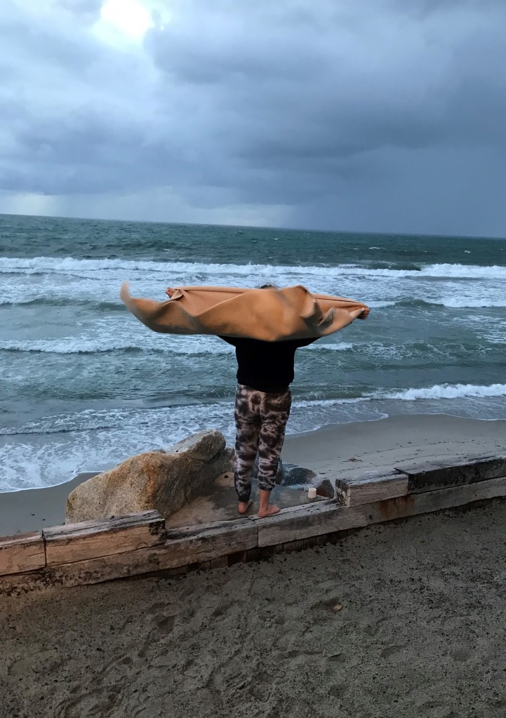 "Releasing that fight can be so much harder than it sounds."
Photograph of a girl standing before the Pacific Ocean, wind blowing a blanket back behind her like a cape. 